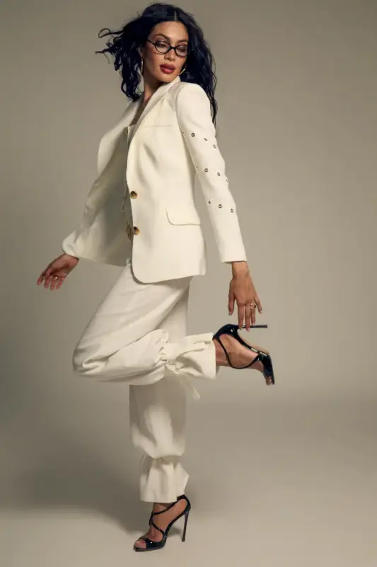 Jane B blazer fusiona la sastrería clásica con un toque contemporáneo lleno de carácter. Confeccionada en un elegante tono crudo, presenta una silueta estructurada que realza la figura con líneas limpias y hombros definidos. Diseñada con cierre frontal de botonadura sencilla, solapas clásicas y bolsillos con solapa, destaca por los delicados ollados metálicos en color oro aplicados a lo largo de las mangas, que aportan un contraste sofisticado y moderno. Su corte ligeramente entallado estiliza la silueta y la convierte en una pieza versátil y favorecedora. Perfecta para llevar con el pantalón a juego y crear un traje impecable, o combinada con denim y prendas más relajadas para un look equilibrado entre elegancia y actitud. Una blazer atemporal reinventada con un sutil espíritu audaz.